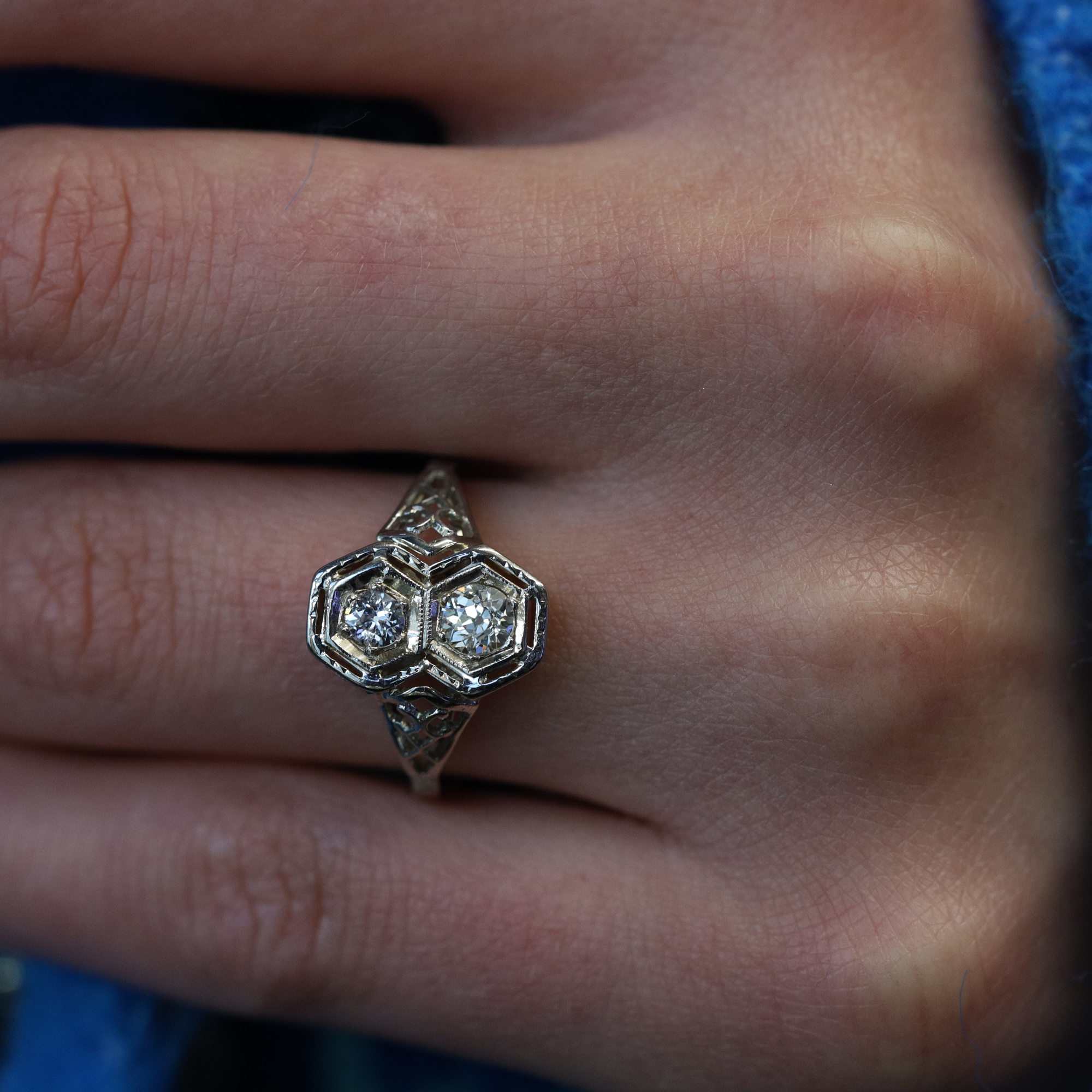 An image of a Rachel Koen brand ring with diamonds for women, worn on a finger and shown in a close-up view. The ring features a hexagonal design with multiple sparkling diamonds set in a detailed white gold band. The photo is taken from a top-down angle, focusing on the ring at a moderate distance, providing a clear view of the ring's intricate details and the diamonds' brilliance. The background is softly blurred, emphasizing the ring on the skin.The ring is pre owned in a good condition. 