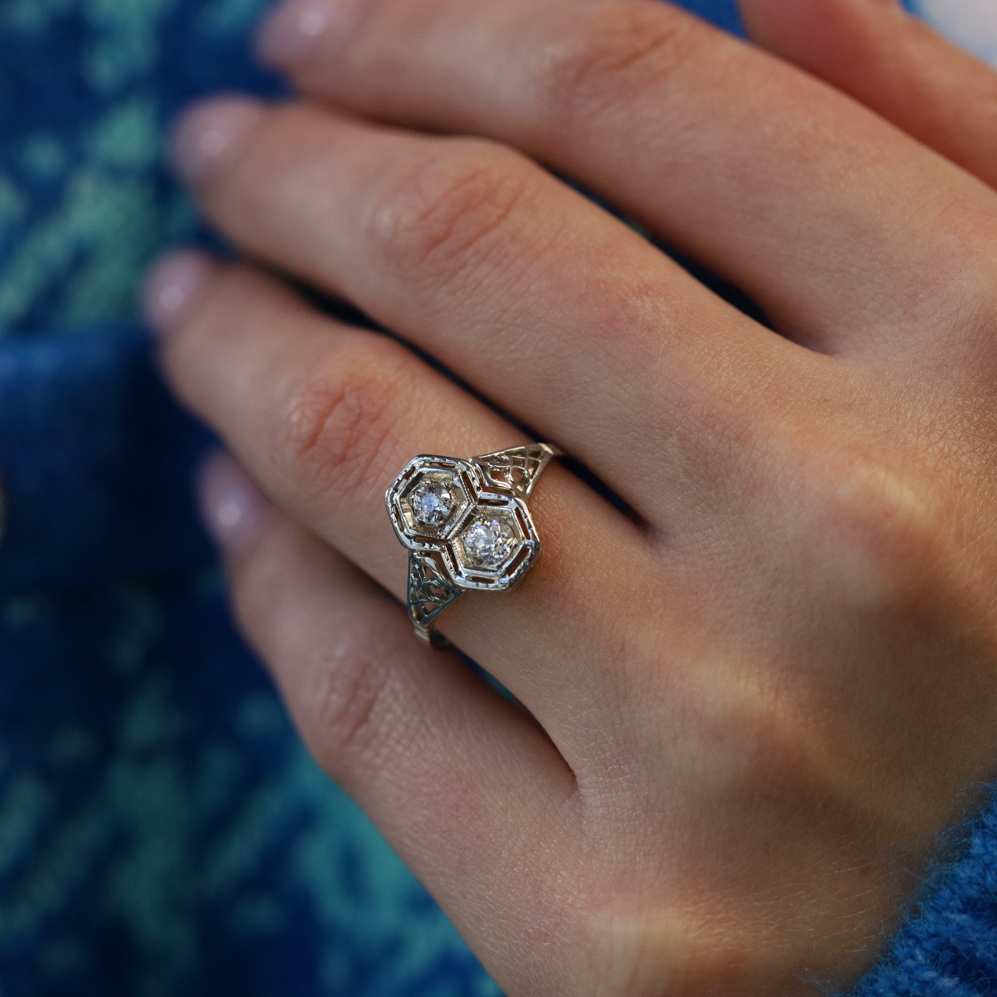 An image of a Rachel Koen brand women's ring with diamonds, displayed on a person's finger. The ring, captured in close-up, is positioned at an angle that highlights the intricate design and the sparkling diamonds set in a metallic band. The view is from a slight elevation, providing a clear view of the ring's top and side details. The focus is on the ring, with the background softly blurred, emphasizing the jewelry's craftsmanship and shine.The ring is pre owned in a good condition. 