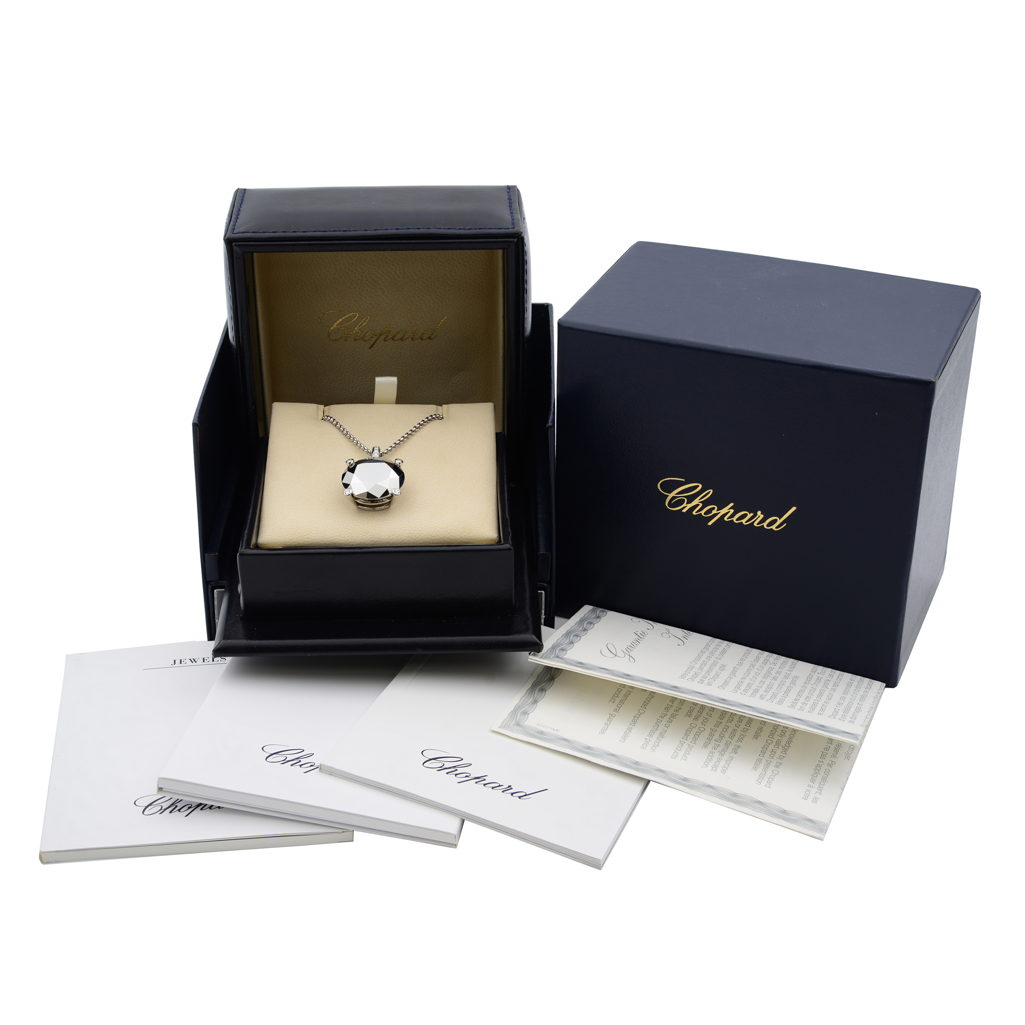 An image of a Chopard necklace with diamonds and gemstones, displayed centrally in an open black jewelry box with a beige interior. The necklace is positioned at the center, showcasing its pendant. The box is placed on a flat surface, surrounded by Chopard-branded booklets and documentation. The angle is slightly elevated, capturing the entire presentation from a short distance. Excellent pre-owned condition. 