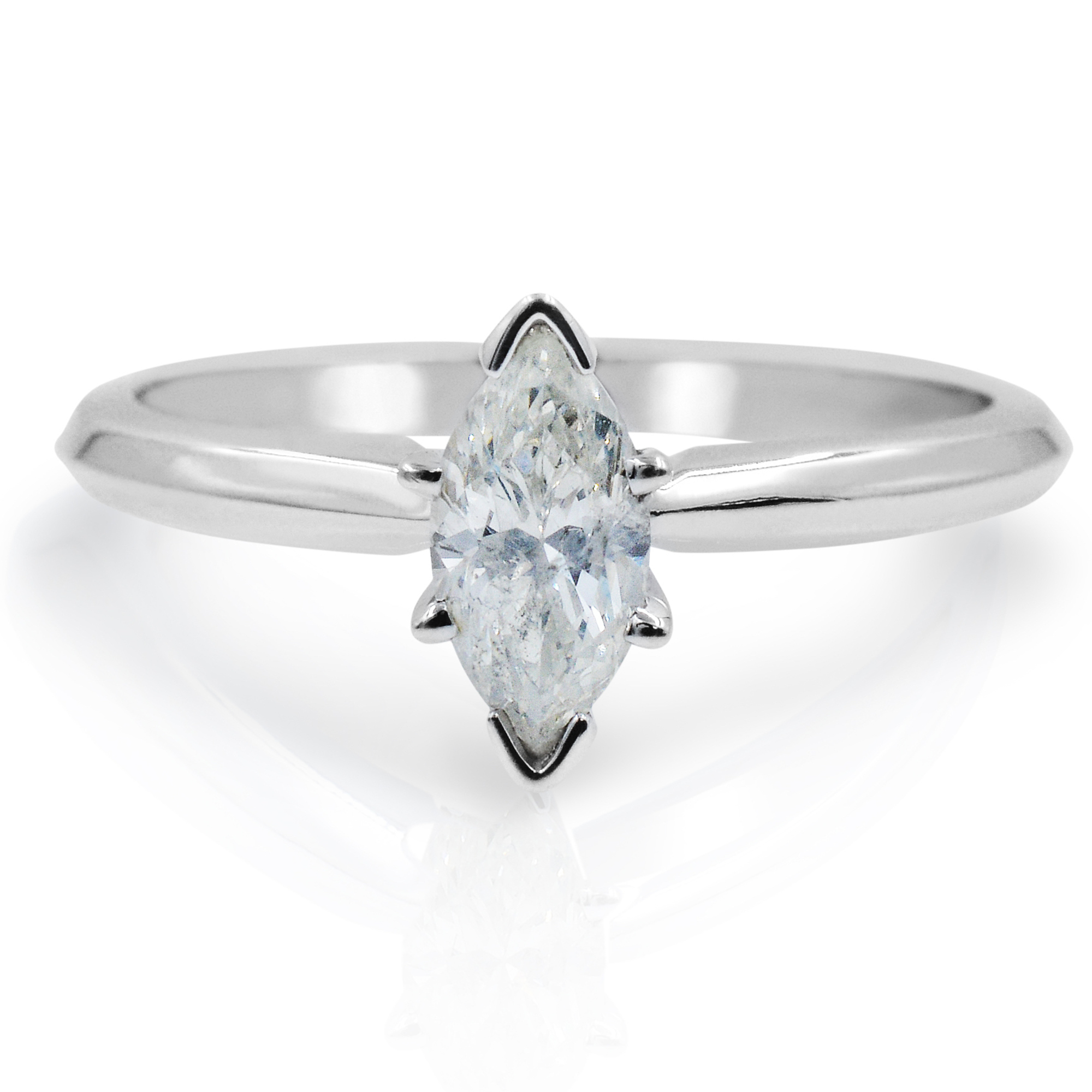 An image of a Rachel Koen brand women's engagement ring with diamond, featuring a close-up front view. The ring is centered with the focus on a marquise-cut solitaire diamond set in a north-south orientation on a polished white band. The angle of the shot and the lighting create a reflection of the ring on the surface below it, suggesting the ring is placed on a reflective surface at a slight distance, emphasizing the diamond's sparkle and the band's shine.