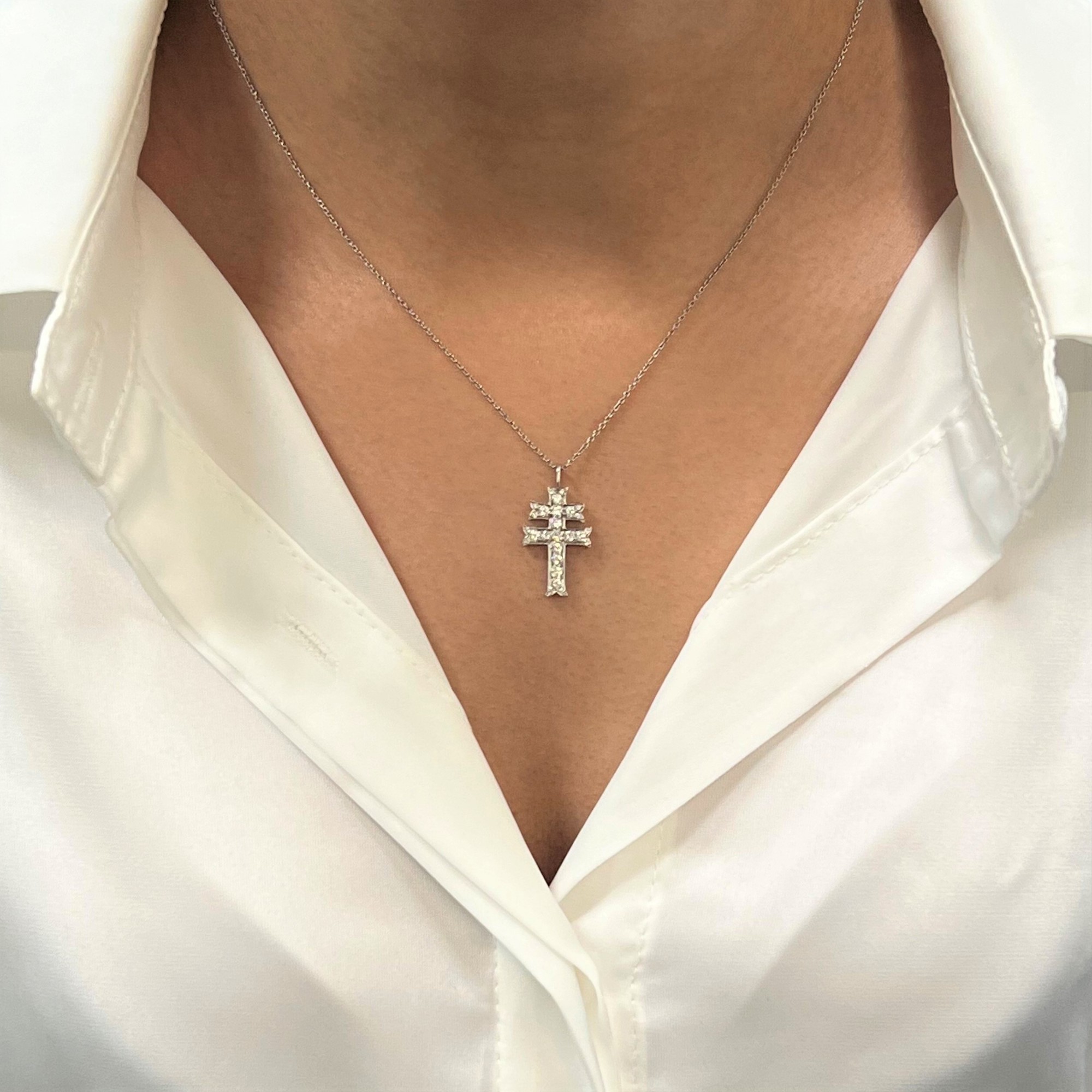 An image of a necklace with diamonds, designed by Rachel Koen, displayed on a woman's neck. The necklace features a cross-shaped pendant encrusted with diamonds, hanging from a delicate chain. The shot is taken from a close-up frontal angle, capturing the necklace centered against a white collared shirt.Excellent pre-owned condition. 