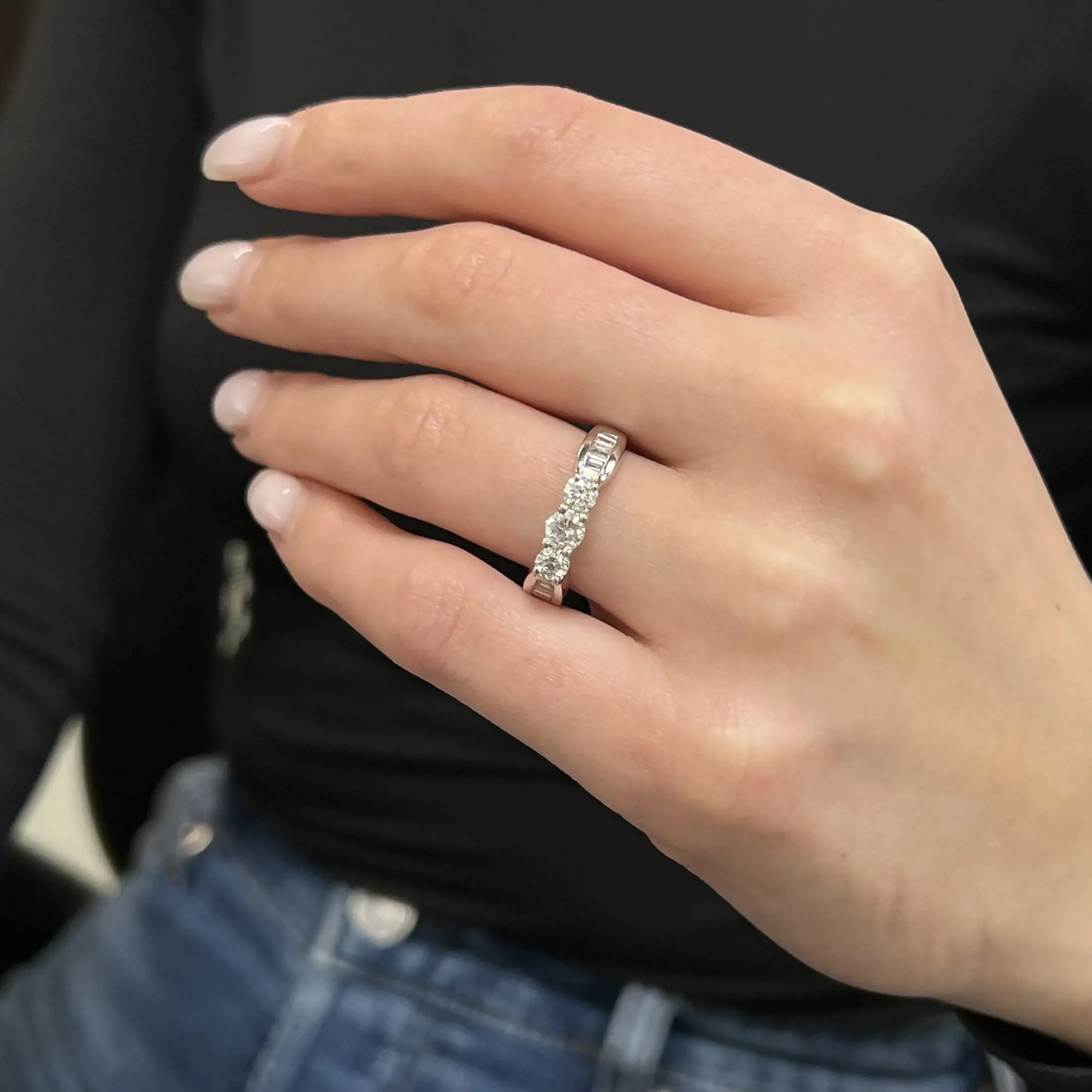 An image of a Rachel Koen women's ring with diamonds, showcased on a person's ring finger. The ring is displayed in a close-up view at a slight angle, emphasizing the sparkle of the diamonds. The person's hand is gently resting against a black backdrop, providing contrast and focus on the ring. The distance is close enough to reveal the details of the ring's design and the shimmering diamonds around the band.The ring is pre-owned in a great condition. 