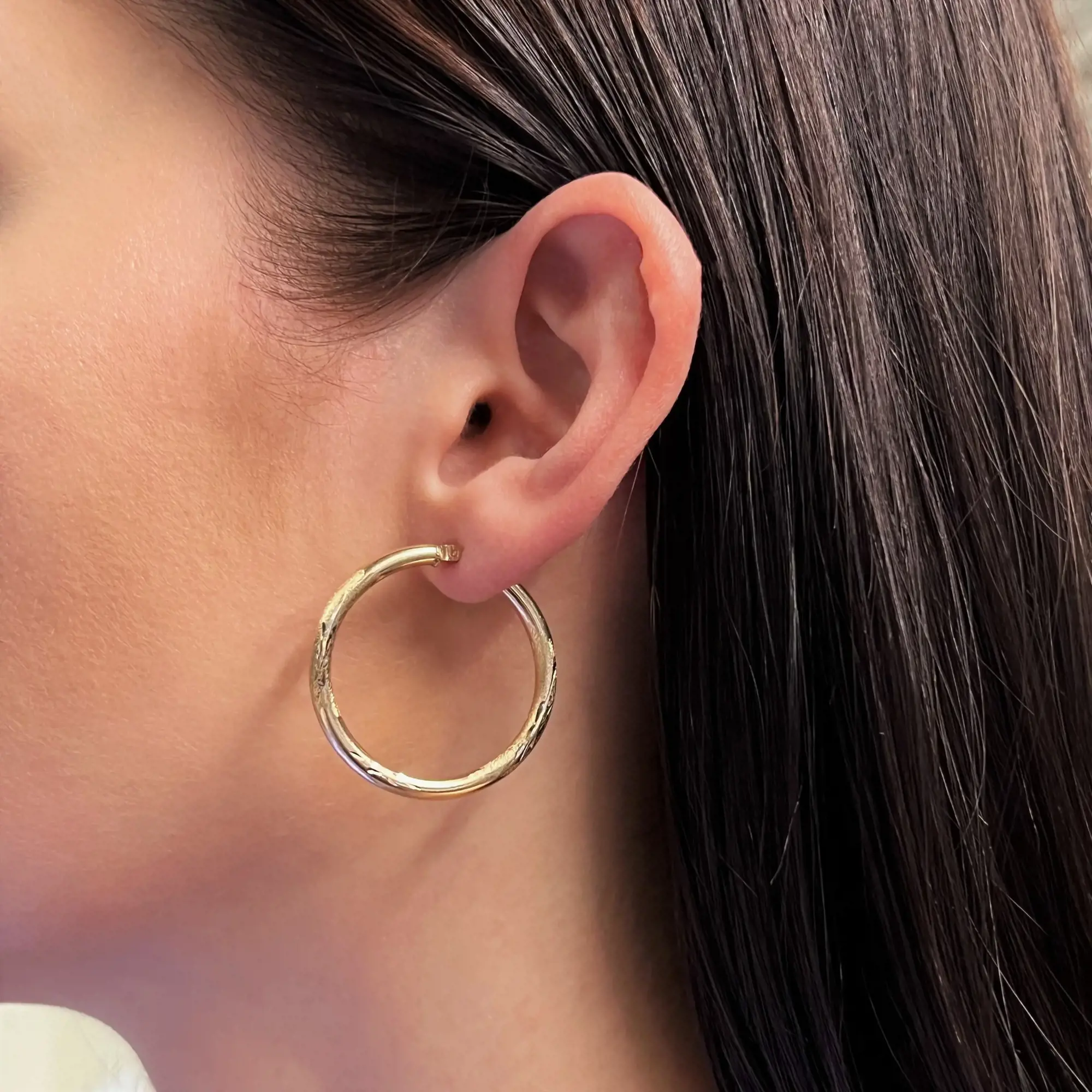An image of a woman's ear adorned with a gold hoop earring, viewed from the side. The earring is smooth and circular, without any stones, and positioned close to the ear. The image is taken at a close angle, highlighting the earring's simple and elegant design against the background of straight dark hair.Excellent pre-owned condition. 