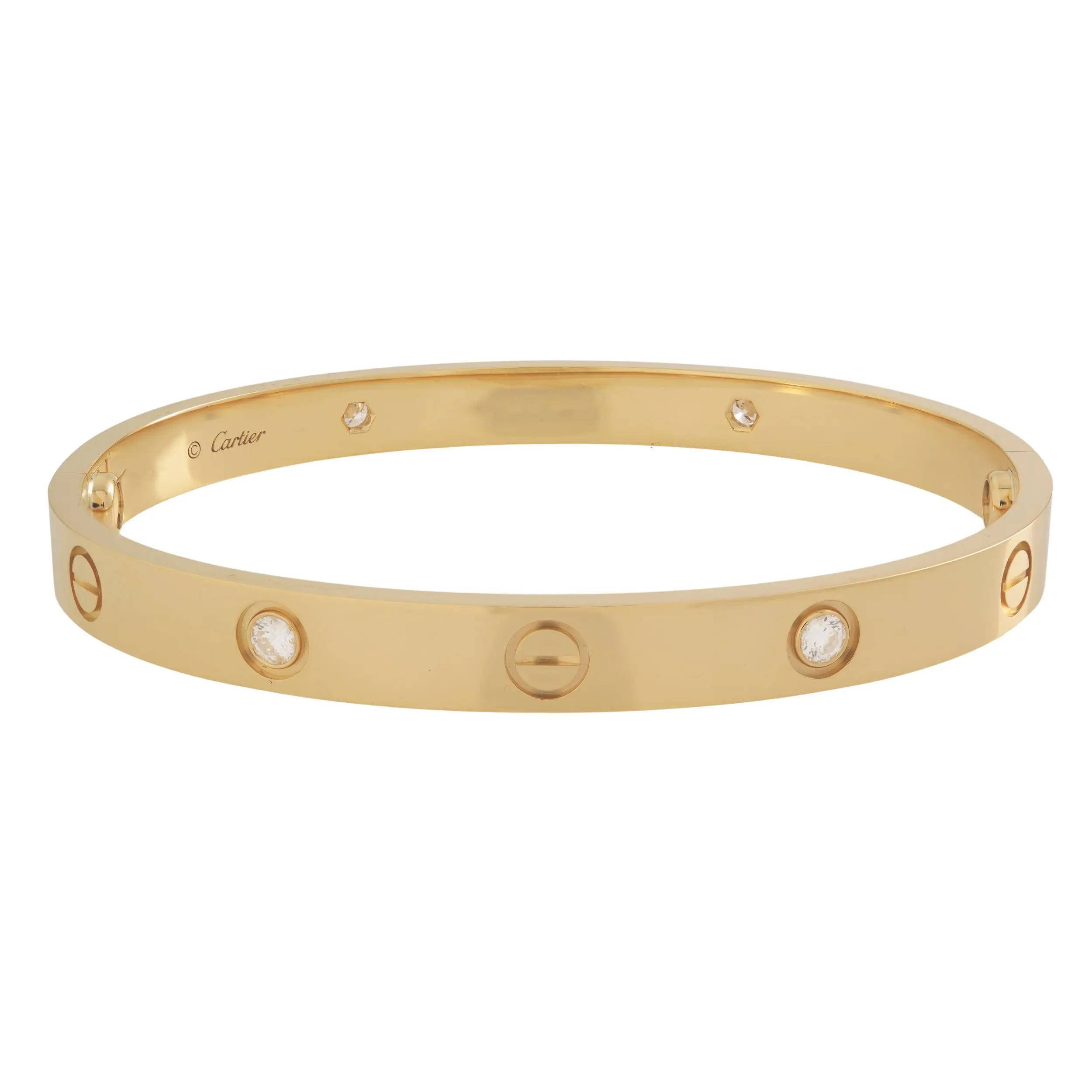An image of a Cartier love unisex adult bracelet with diamonds, positioned centrally and viewed from a front angle. The bracelet is displayed against a neutral background, allowing a clear view of its yellow gold surface and the multiple diamonds encrusted along its band. The photo is taken from a close distance, showing the bracelet's details and the brand name inscribed on it. Great preowned condition.