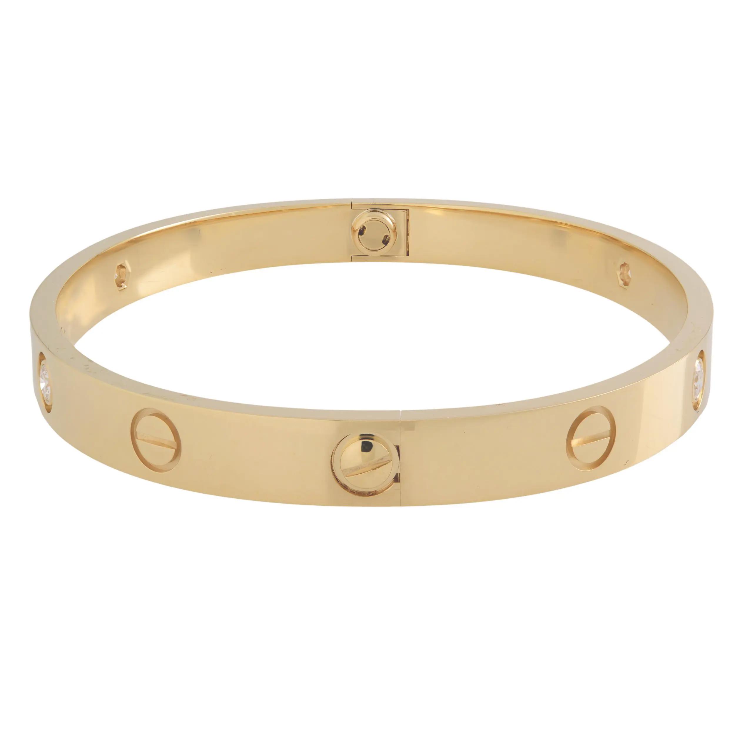 An image of a Cartier love unisex adult bracelet with diamonds, displayed in a straight-on view at eye level. The bracelet is a yellow gold bangle with a smooth, polished finish, featuring a series of evenly spaced decorative screws and four embedded diamonds. The diamonds catch the light and are set flush with the surface of the bracelet. The background is a neutral, light color that contrasts with the warm gold of the bracelet, which is centered and occupies a majority of the frame. Comes in great preowned condition.