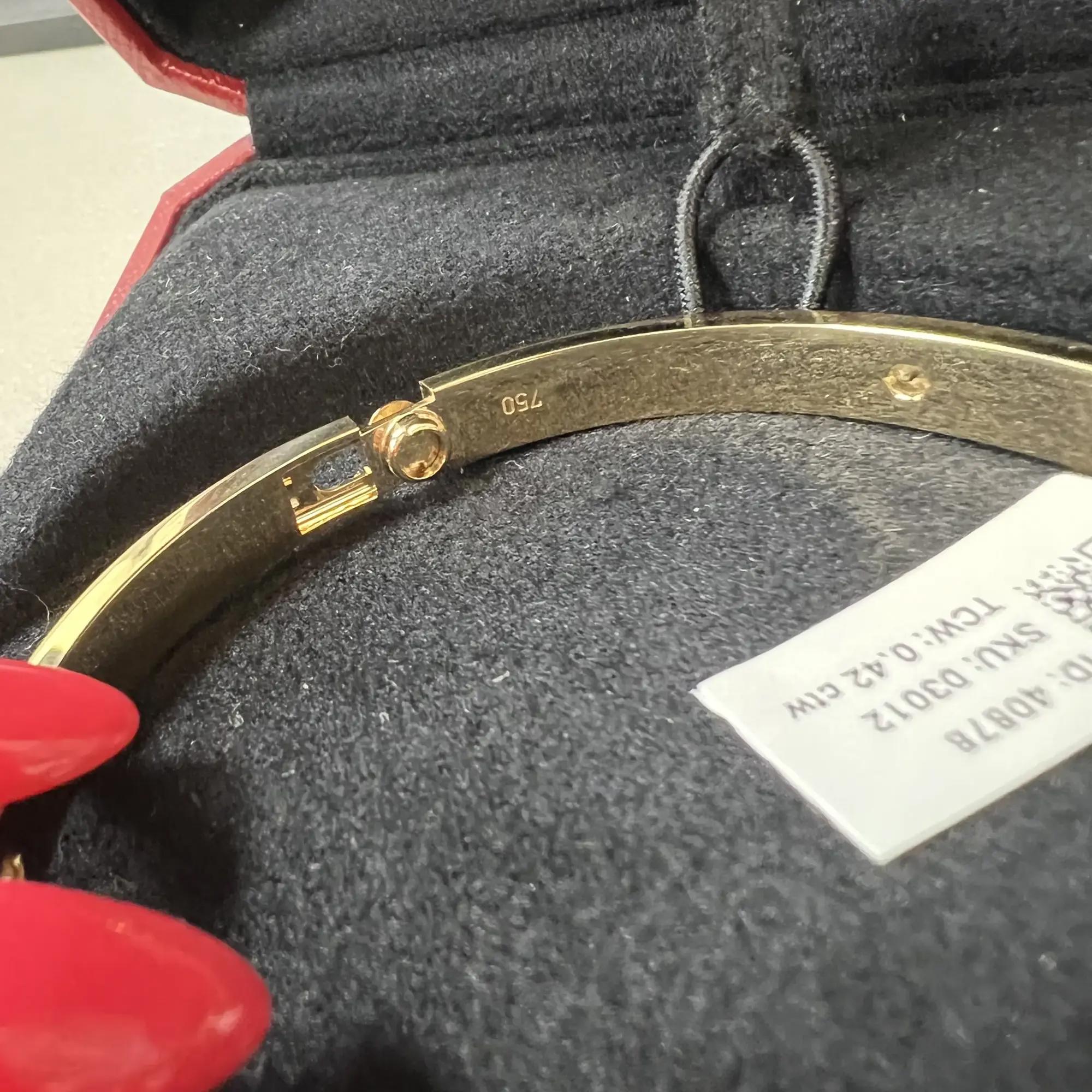 An image of a Cartier love bracelet with diamonds, displayed at a close-up angle within a red jewelry box. The bracelet, intended for unisex adults, is positioned diagonally across the frame, with its clasp slightly open towards the top right corner. It features a polished yellow gold finish with multiple diamonds inset. The bracelet rests on a black velvety surface, and the view is from above, highlighting the reflective quality of the gold and the sparkle of the diamonds. Comes in a great preowned condition.