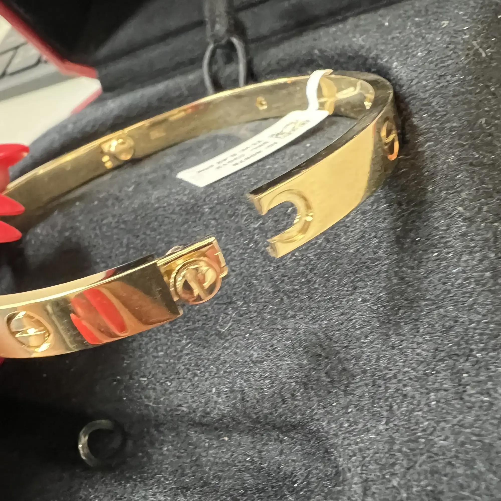 An image of a Cartier love unisex bracelet with diamonds, displayed at a close diagonal angle showcasing its elegant design. The bracelet is positioned against a dark background, with the focal point being the yellow gold bracelet featuring the iconic screw motifs and shimmering diamonds interspersed around the circumference. The bracelet's shiny surface reflects the ambient light, highlighting its luxurious appeal. Comes in a great preowned condition.