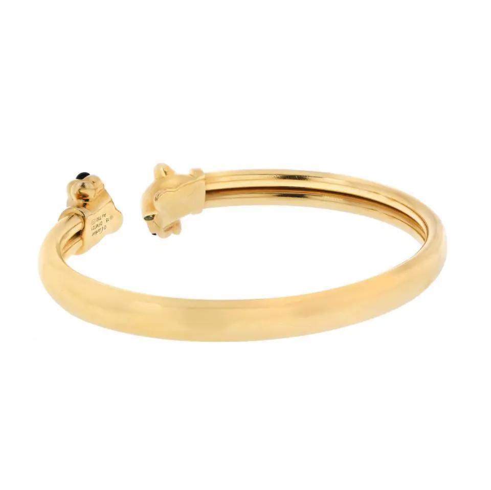 An image of a Cartier unisex adult bracelet with gemstones, shown in a close-up, head-on view against a white background. The bracelet is made in yellow gold, with a sleek and polished finish. It features a design with two ends not meeting, each capped with a panther head adorned with gemstones for eyes and nose. The bracelet is positioned horizontally in the center of the frame, allowing a clear view of the details and craftsmanship. Great preowned condition.