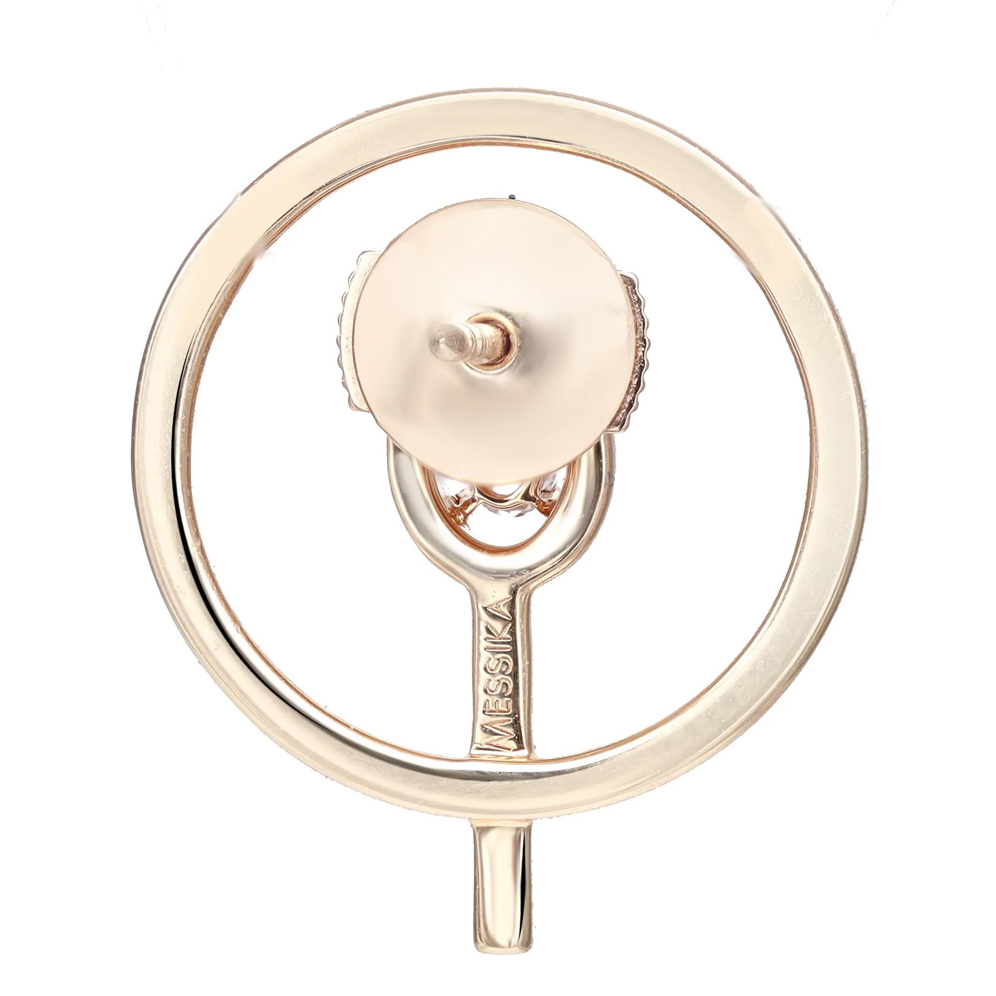 An image of a Messika brand earring for women, featuring a circular design with diamonds. The earring is captured up close from a frontal angle, showcasing its polished surface and the engraved brand name at the bottom. The piece is centered and occupies the majority of the frame, set against a plain background for a clear view of its details.