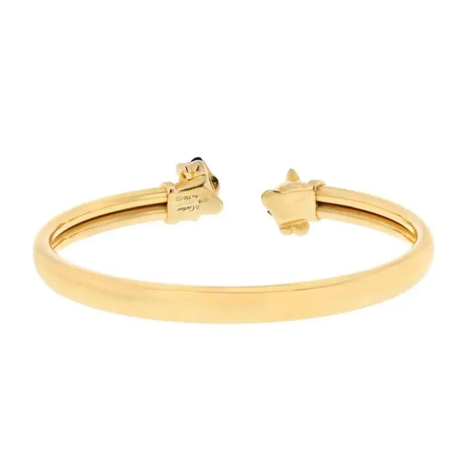 An image of a Cartier unisex adult bracelet with gemstones. The bracelet is photographed from a back angle against a white background, showcasing its entire form. It features a sleek, yellow gold open bangle with visible engraving of the brand's hallmark and other details. On the right end, a star-shaped gemstone embellishment is prominently displayed. The bracelet is centered and occupies a middle ground position, allowing for a clear and detailed view of its design and craftsmanship. Great preowned condition. 