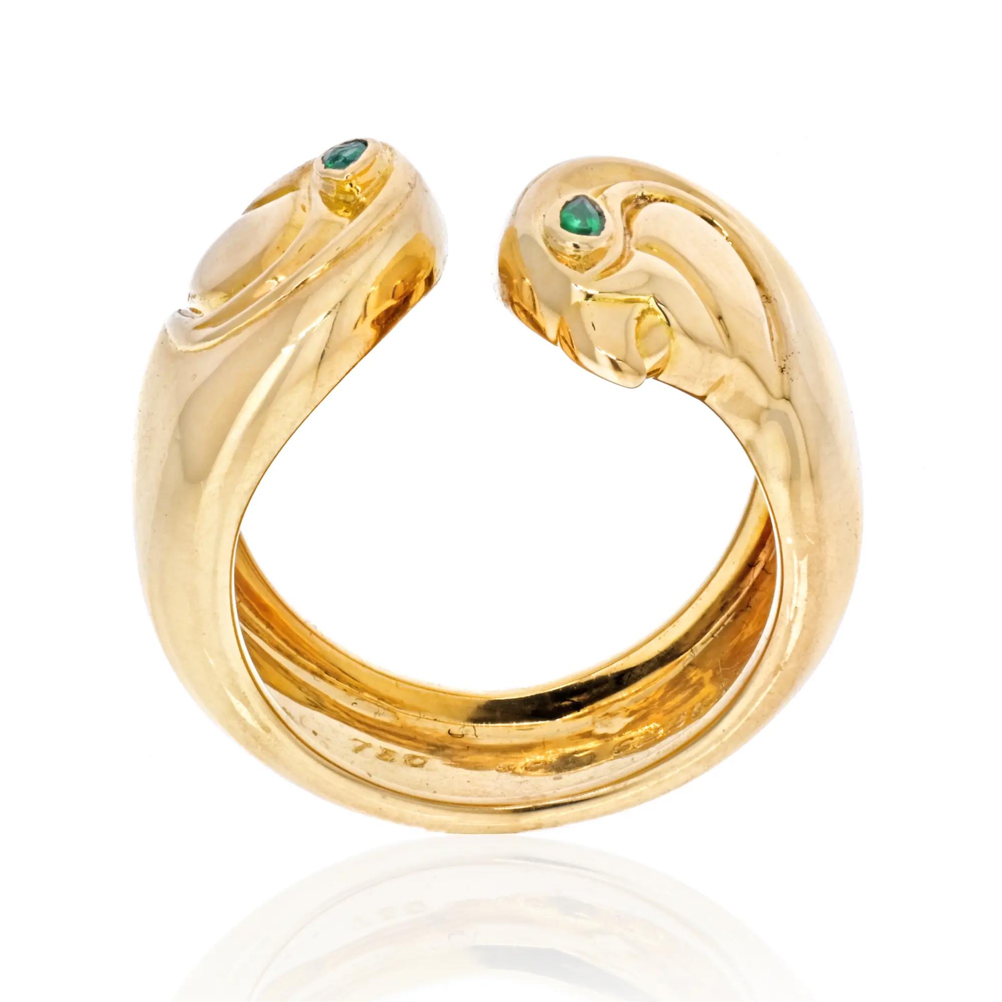 An image of a women's Vintage Cartier Anoubois ring with gemstones, showcasing an open design with two small green gemstones set at the ends of the yellow gold band. The front view of the ring is centered and shot at a straight angle, with high resolution capturing the gleaming metal and the clear detail of the green gemstones. The ring occupies the middle ground, providing a clear view of its unique design and the hallmark inside the band. Comes in a great preowned condition.