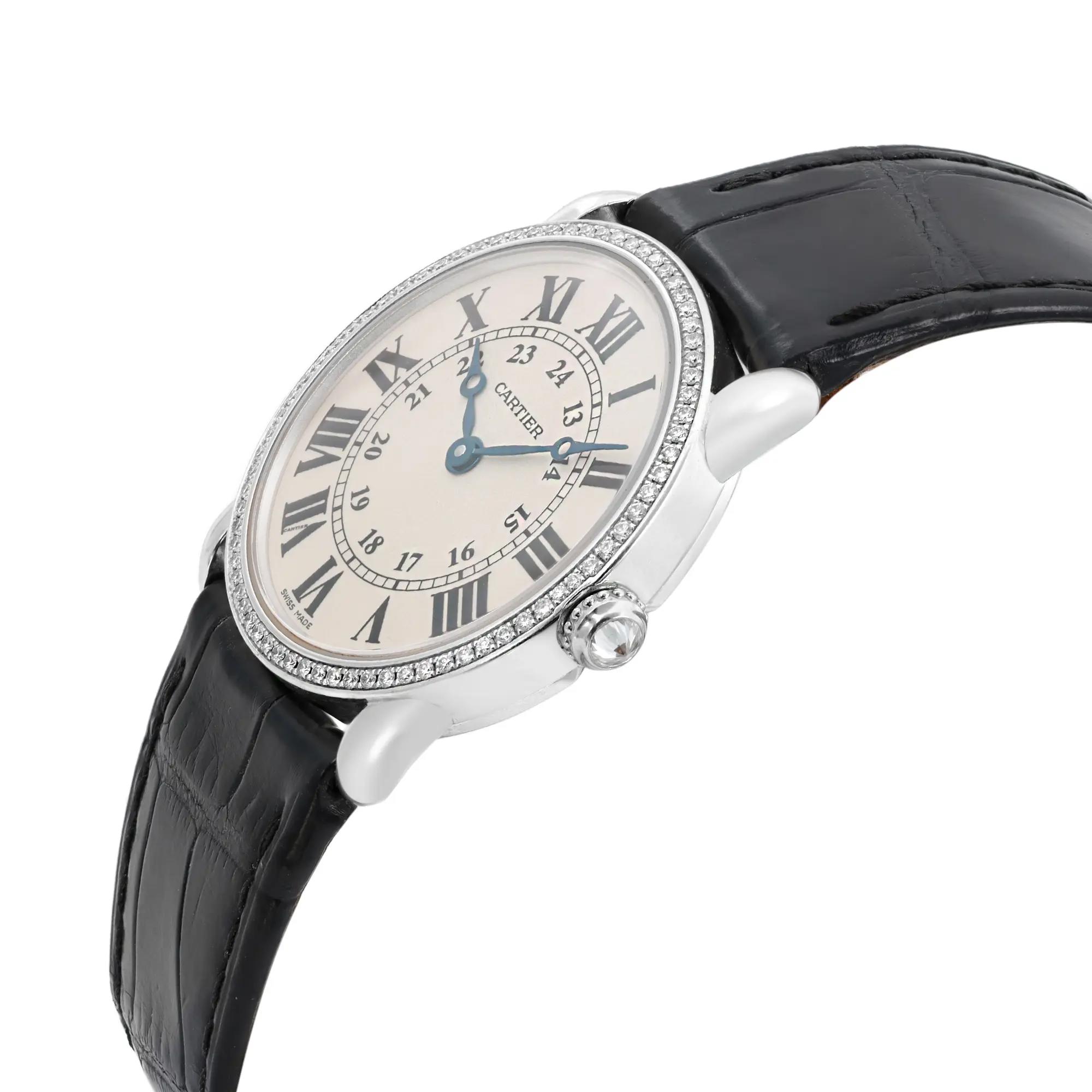 An image of a pre-owned wristwatch shown from a side profile view, highlighting the crown on the right side. The watch has a round face with Roman numerals and blue hands, encircled by a bezel adorned with small stones. The case is silver, and the strap is black with a textured pattern. The angle captures the watch at a slight upward tilt, showcasing its elegant design from a close distance.