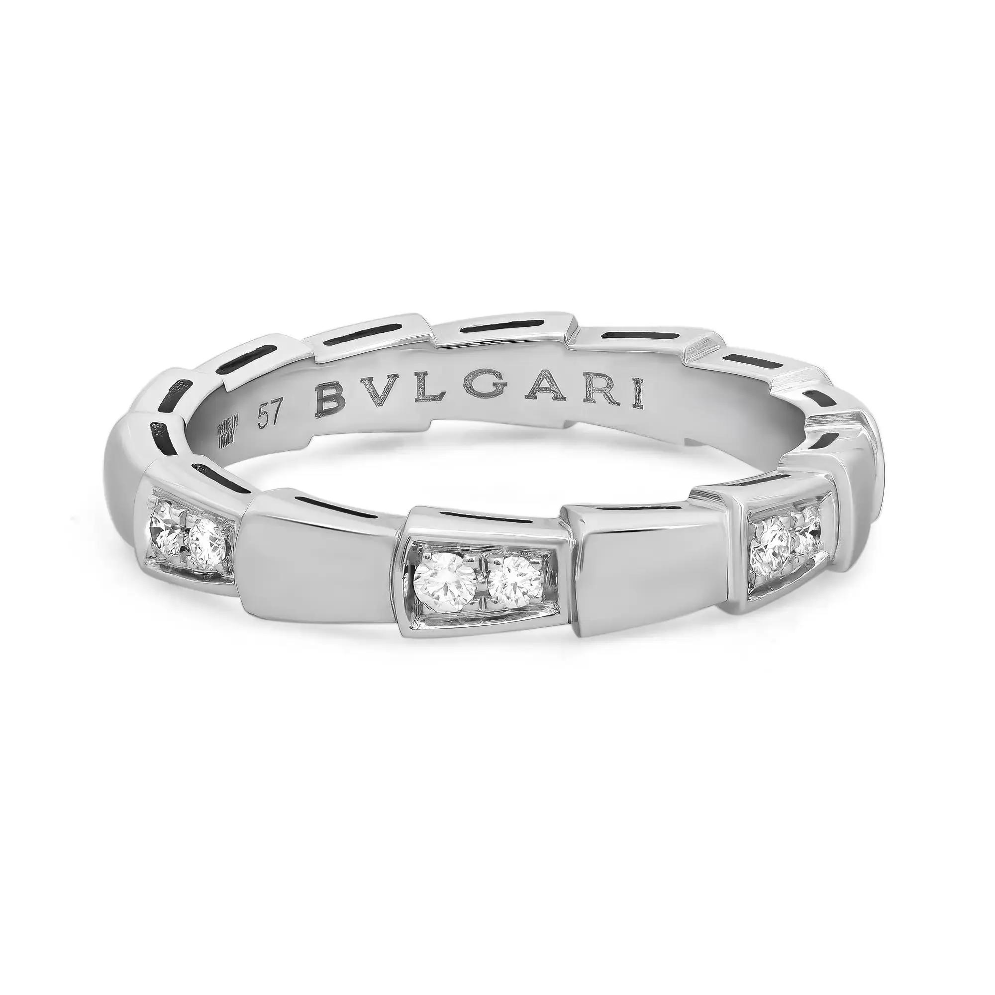 An image of a Bvlgari Serpenti Viper unisex adult band ring with diamonds, displayed in a close-up, front-facing view. The ring features a sleek, white gold band with cut-out details. Across the band, the brand name "BVLGARI" is engraved with prominence. The ring is adorned with multiple sparkling diamonds, bezel-set in a symmetrical alignment that accentuates their brilliance. The diamonds are positioned at equal intervals along the band, with the design allowing for the stones to capture and reflect light effectively. The image is taken from a slightly elevated angle to showcase the ring's details and the reflective quality of both the diamonds and the metal. The condition of the ring is new. 