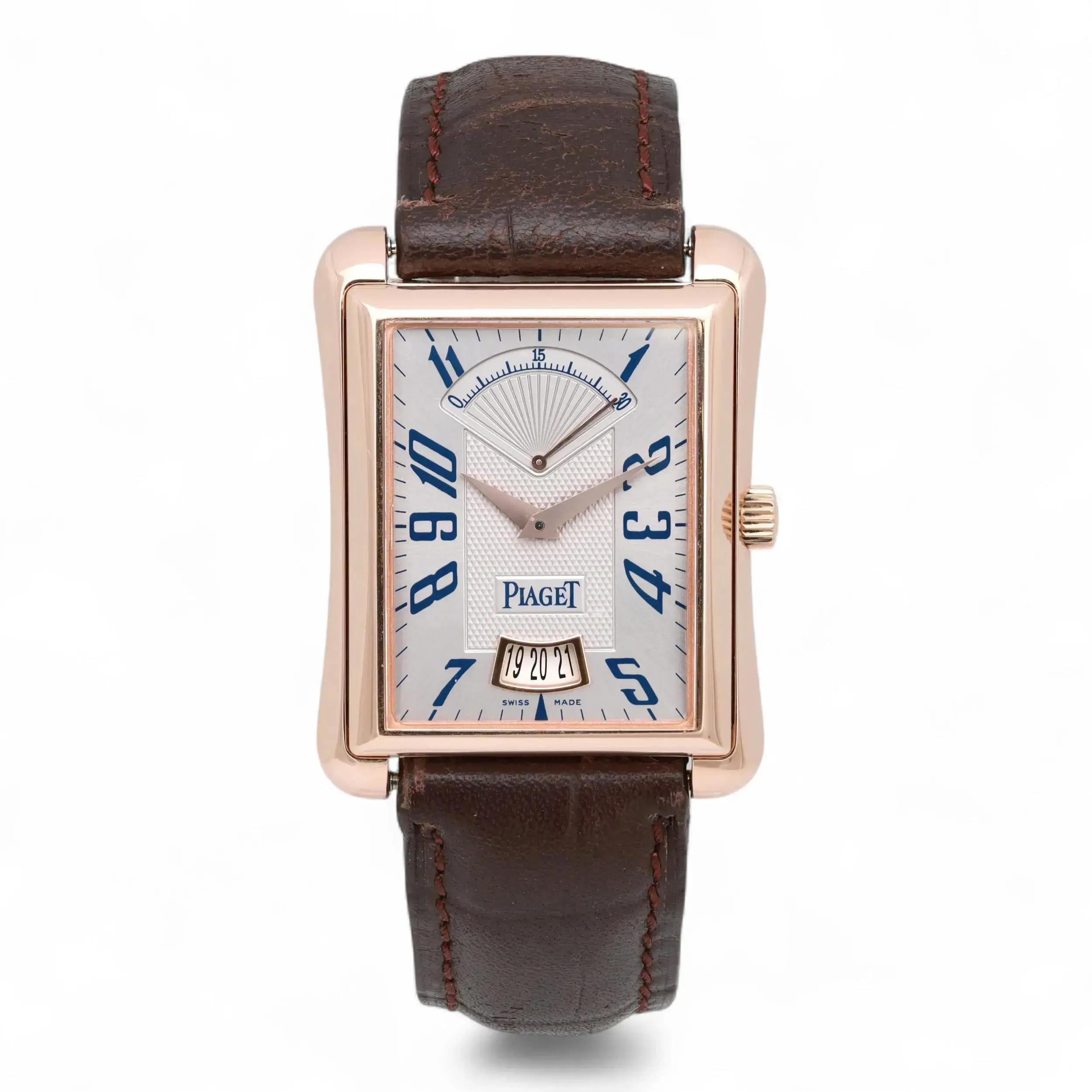An image of a pre-owned men's Piaget Emperador Date Retrograde 18K Rose Gold Silver Dial Watch P10109 positioned upright, facing forward. The watch features a rectangular rose gold case with blue numerals on a silver dial. It has a brown leather strap and a date display at the bottom. The image is taken from a straight-on angle at a close distance, highlighting the watch's elegant design and details.