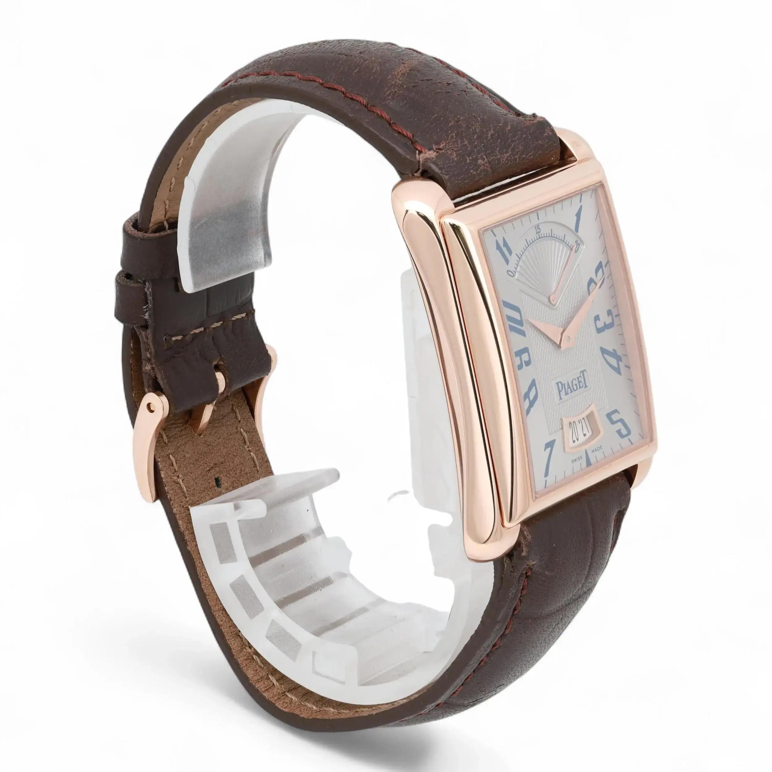 An image of a pre-owned men's Piaget wristwatch positioned at a slight angle, showcasing the side and part of the face. The watch has a rectangular case with a rose gold tone and features a brown leather strap. The watch face displays blue numerals, a date function, and intricate detailing. The angle highlights the watch’s elegant curves and craftsmanship, with the strap partially buckled. The photo is taken from a close distance, focusing on the watch’s design and materials.